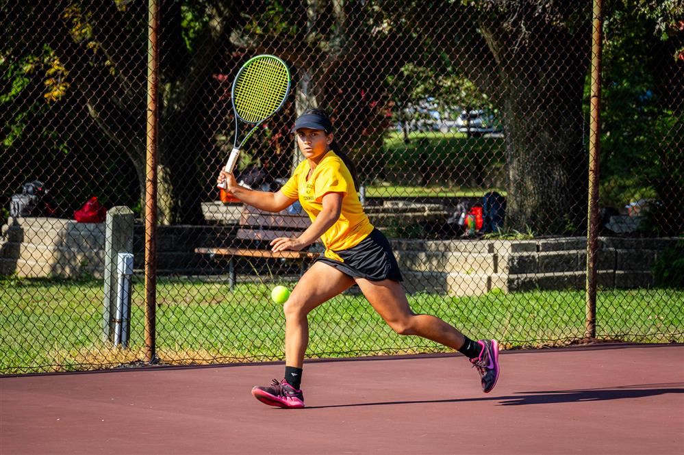 Student volleys a ball across a tennis court in a yellow shirt.